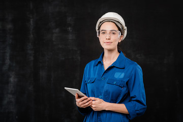 Pretty young specialist in hardhat and blue workwear using touchpad in isolation