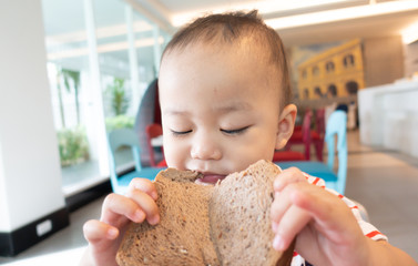 Wall Mural - Little asian boy eating whole wheat bread at home.2 years old baby boy enjoy eating with bread slice in breakfast time.