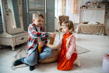 Boy and baby girl drink natural juice at home in a large bright living room. Natural orange juice in a glass. healthy products, joyful children. Bright christmas scenery. New Years is soon.