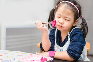 Wall Mural - Little asian girl eating dragon fruit at home.Cute toddler girl eating biting on dragon fruit with fork.Delicious fruit and Enjoy eating concept.