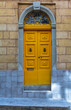 Historical ornate wooden yellow door in a stone entry in Bormla, Malta. With glass window above. Architectural theme.