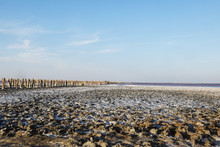 Salt Lake In Crimea In Summer, Salt Crystallizes And Shimmers Pink In The Sun. In The Distance, Barely Visible Wooden Poles Are All In The Mud And Trails Of Tourists.