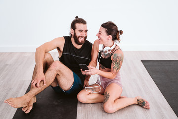 two friends at the gym listening to music on mobile phone and headset and having fun. Sport and technology concept