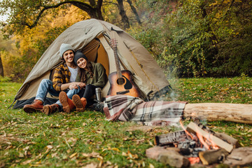 Young loved couple of tourists have a date in the forest. Attractive young woman and handsome man are spending time together on nature. Hugging lovers near campfire.