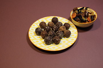 Canvas Print - Energy balls dessert in colorful plate made of dried fruits, cocoa, sesam seeds on brown background