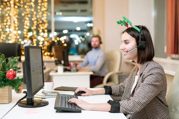 Poster - Happy young operator in xmas headband and headset shopping online by workplace