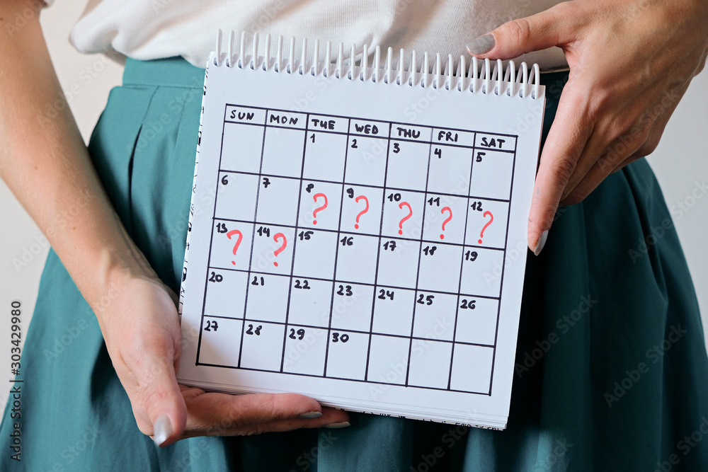 Woman holding calender with marked missed period. Unwanted pregnancy, woman's health and delay in menstruation. - obrazy, fototapety, plakaty 