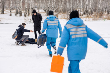 Wall Mural - Rear view of paramedics in blue uniform hurrying to sick person lying in snow