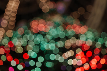 Illuminated abstract round red, orange, green and gold bokeh on dark background. Colourful glitter bokeh from out of focus view of decoration bulbs.