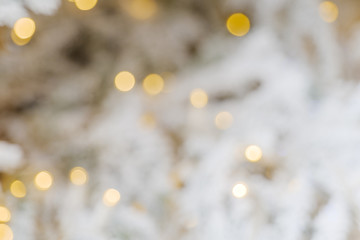 Wall Mural - Defocus close up view of Illuminated abstract round gold bokeh on blur white background. Golden glitter bokeh from out of focus view of decoration bulbs on white Christmas tree.