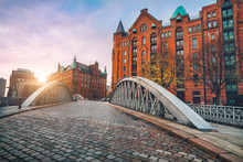 Arch Bridge Over Alster Canals With Cobbled Road In Historical Speicherstadt Of Hamburg, Germany, Europe. Scenic View Of Red Brick Building Lit By Golden Sunset Light