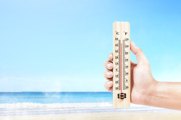 Wall Mural - Hand holding thermometer measuring the temperature on the beach with a blue sky background