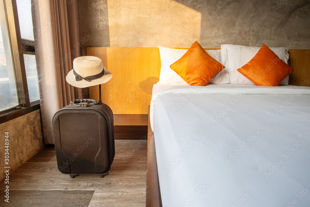 A suitcase with hat in comfortable hotel bedroom. - obrazy, fototapety, plakaty 