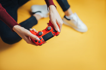 Wall Mural - Young thin woman playing with red gamepad, sitting on yellow background. flat lay.