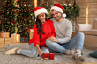 © New Africa - Happy young couple wearing Santa hats in living room decorated for Christmas