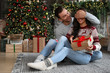 © New Africa - Happy couple with gift box in living room decorated for Christmas