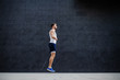 © Dusan Petkovic - Side view of handsome muscular caucasian man in shorts and t-shirt skipping rope in front of gray wall outdoors.