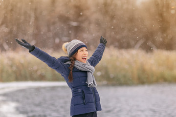 Happy winter snow fun Asian woman playing outside in snowfall enjoying falling snowflakes cold winter weather outdoors in nature forest healthy people lifestyle. Woman wearing hat, gloves ,coat.