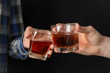 Male hands holds glasses with whiskey on black background. Cheers, close up