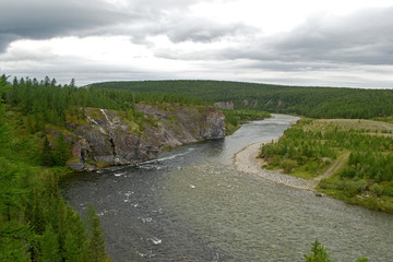 View from the high bank to the bend of the northern mountain river Kozhim. A high cliff on one side of the river and a gentle wooded shore on the other side. Subpolar Ural, Yugyd Va National Park