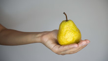 Hand Of A White Woman Holding Yellow Pear On A Grey Background.