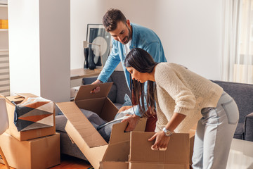 Smiling young couple move into a new home carrying boxes of belongings.