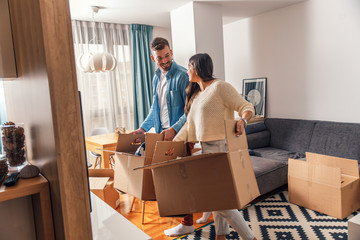 smiling young couple move into a new home carrying boxes of belongings.