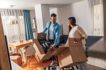 Wall Mural - Smiling young couple move into a new home carrying boxes of belongings.