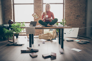 Wall Mural - Full body photo of happy trader woman sit on table crossed legs feel carefree careless rest relax hold white coffee cup in messy office loft