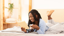 African American Girl Reading Book Lying In Bed At Home
