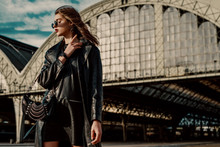 Outdoor Fashion Portrait Of Young Confident Model, Woman Wearing Trendy Black Leather Trench Coat, Dress, Wrist Watch, With Small Hobo Bag, Posing In Street Of City. Copy, Empty Space For Text