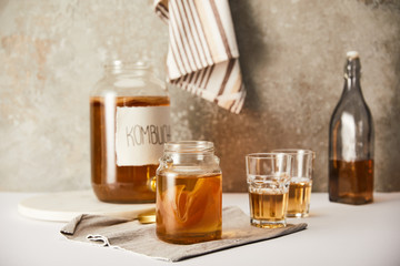 Canvas Print - selective focus of jar with kombucha near glasses on textured grey background with striped napkin