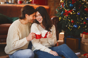 Wall Mural - Couple in love having cocoa next to Christmas tree