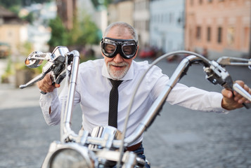 A front view of senior businessman with goggles and motorbike in town.