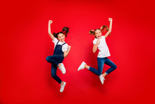 Full Length Photo Of Cheerful Two Small Little People Girlfriends Celebrate Triumph Raise Fists Scream Yes Jump Wear White T-shirt Denim Jeans Sneakers Isolated Bright Color Background