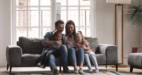 Wall Mural - Happy family of four using smartphone relax on couch