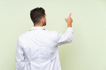 Wall Mural - Young doctor man over isolated green wall pointing back with the index finger