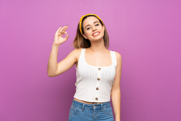 Wall Mural - Pretty young woman over isolated purple wall showing ok sign with fingers