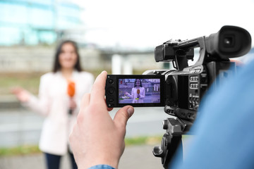 Canvas Print - Young male journalist and video operator working on city street, focus on camera display