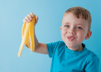 Little Boy Holding and eating an Banana on blue background, food, diet and healthy eating concept