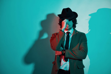 Wall Mural - Portrait of young stylish man in hat, suit and tie that stands in neon lights in the studio