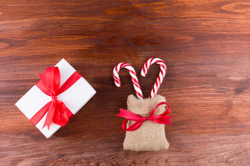 two candy canes with white gift box red ribbinon bow on dark wooden board