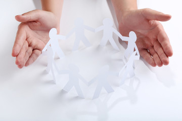 Female hands protecting paper chain people on white background