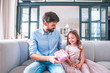 © Afshar Tetyana - adorable girl taking present box from her dad while sitting on the couch in living room