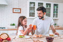 Smiling Father And Daughter Clicking Glasses With Drinking Juice For Breakfast In The Kitchen