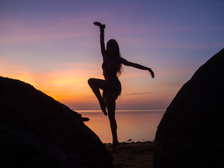 Silhouettes of a woman dancing on the beach on a background of colorful sunset