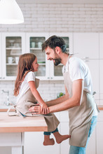 Father And Daughter Wearing Aprons Looking At Each Other On The Domesic Kitchen