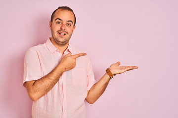 Sticker - Young man wearing elegant shirt standing over isolated pink background amazed and smiling to the camera while presenting with hand and pointing with finger.