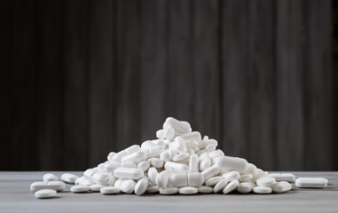 White pills spilled on gray wooden background