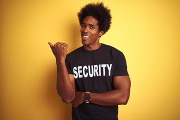 Sticker - American safeguard man with afro hair wearing security uniform over isolated yellow background smiling with happy face looking and pointing to the side with thumb up.